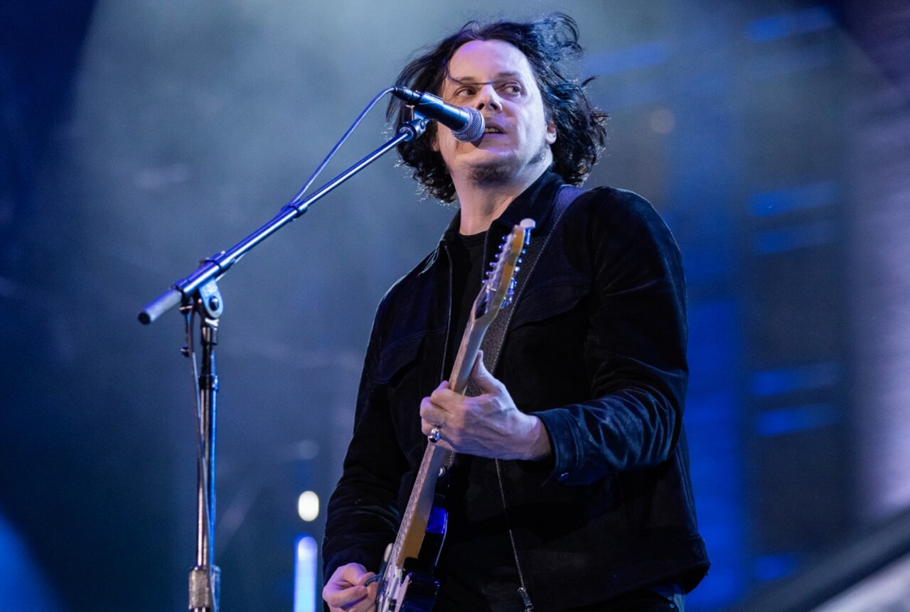 Jack White performing live on stage playing electric guitar.