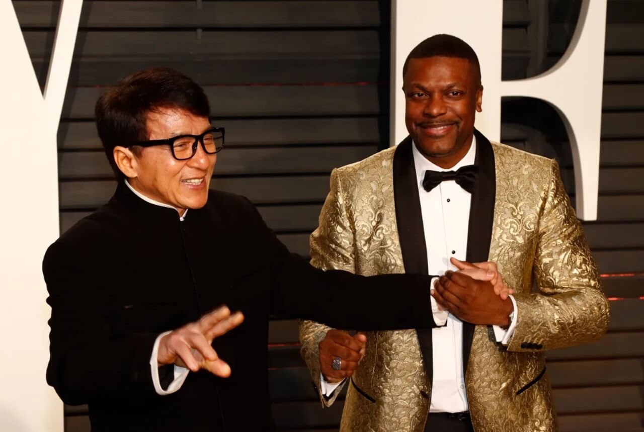Jackie Chan and Chris Tucker together on the red carpet, smiling at fans and photographers.