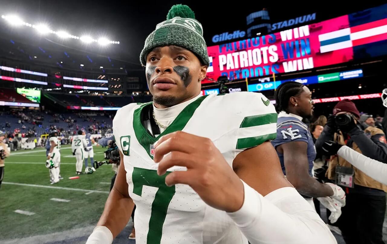 Justin Fields on the Jets sideline after being benched, appearing contemplative during game action.