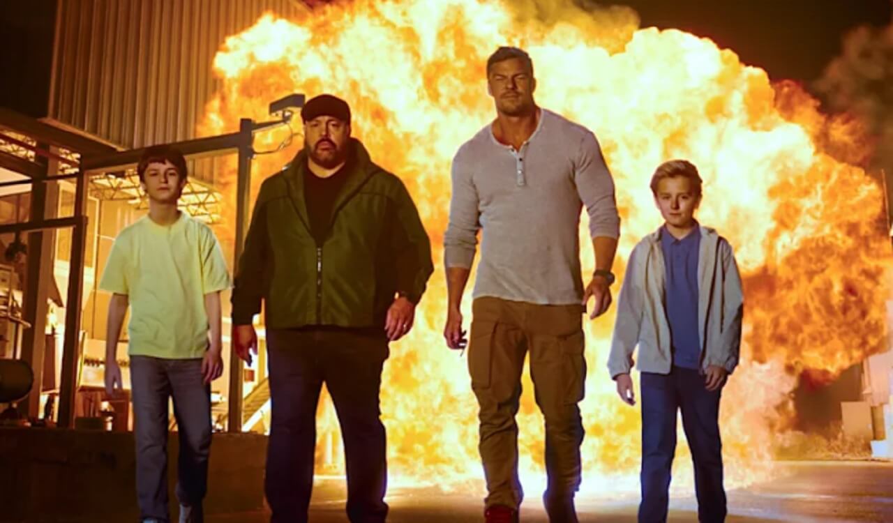 Glen Powell as Ben Richards in Edgar Wright’s The Running Man, standing defiantly in a futuristic game show arena.