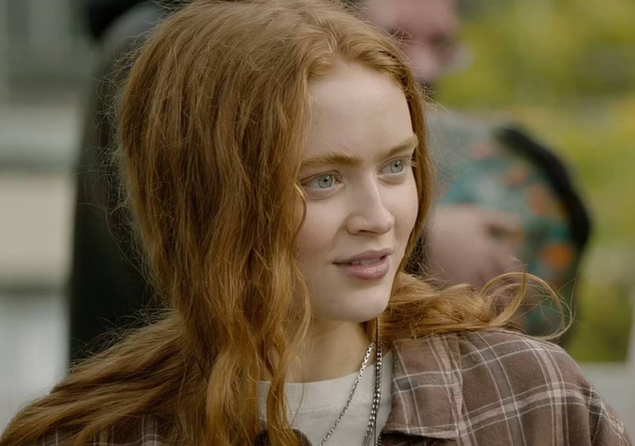 Sadie Sink on the red carpet smiling while posing for photos at a premiere event.