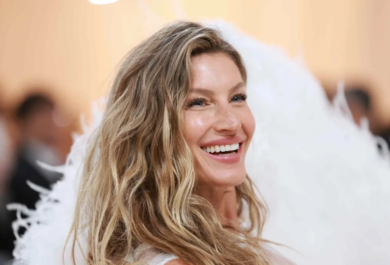 Gisele Bündchen poses at a red carpet event in an elegant white gown.