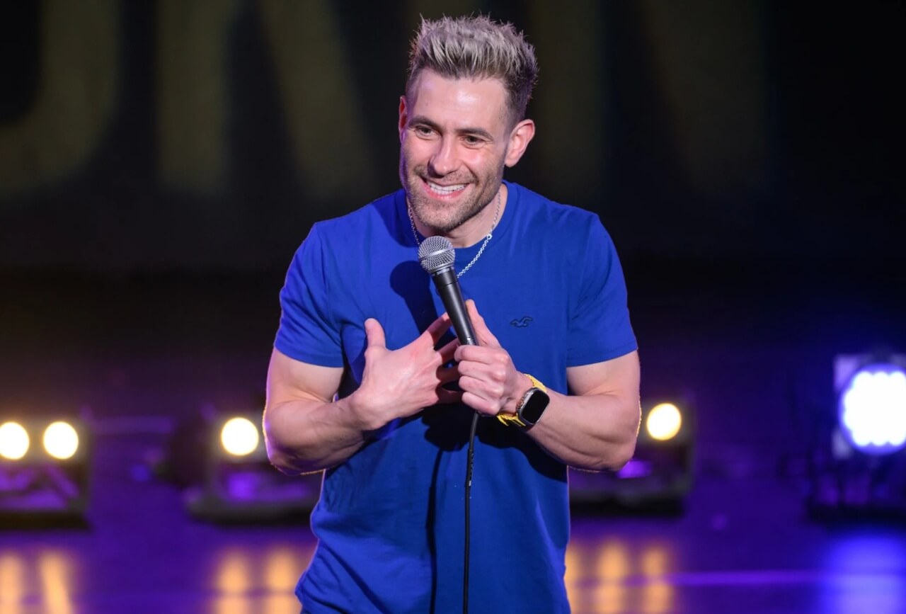 British comedian Simon Brodkin performing stand-up comedy on stage.