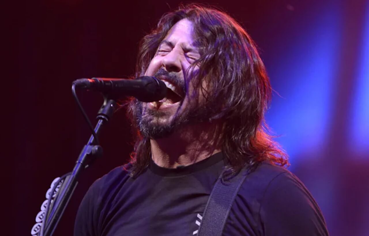 Dave Grohl performing live, holding a guitar under stage lights.