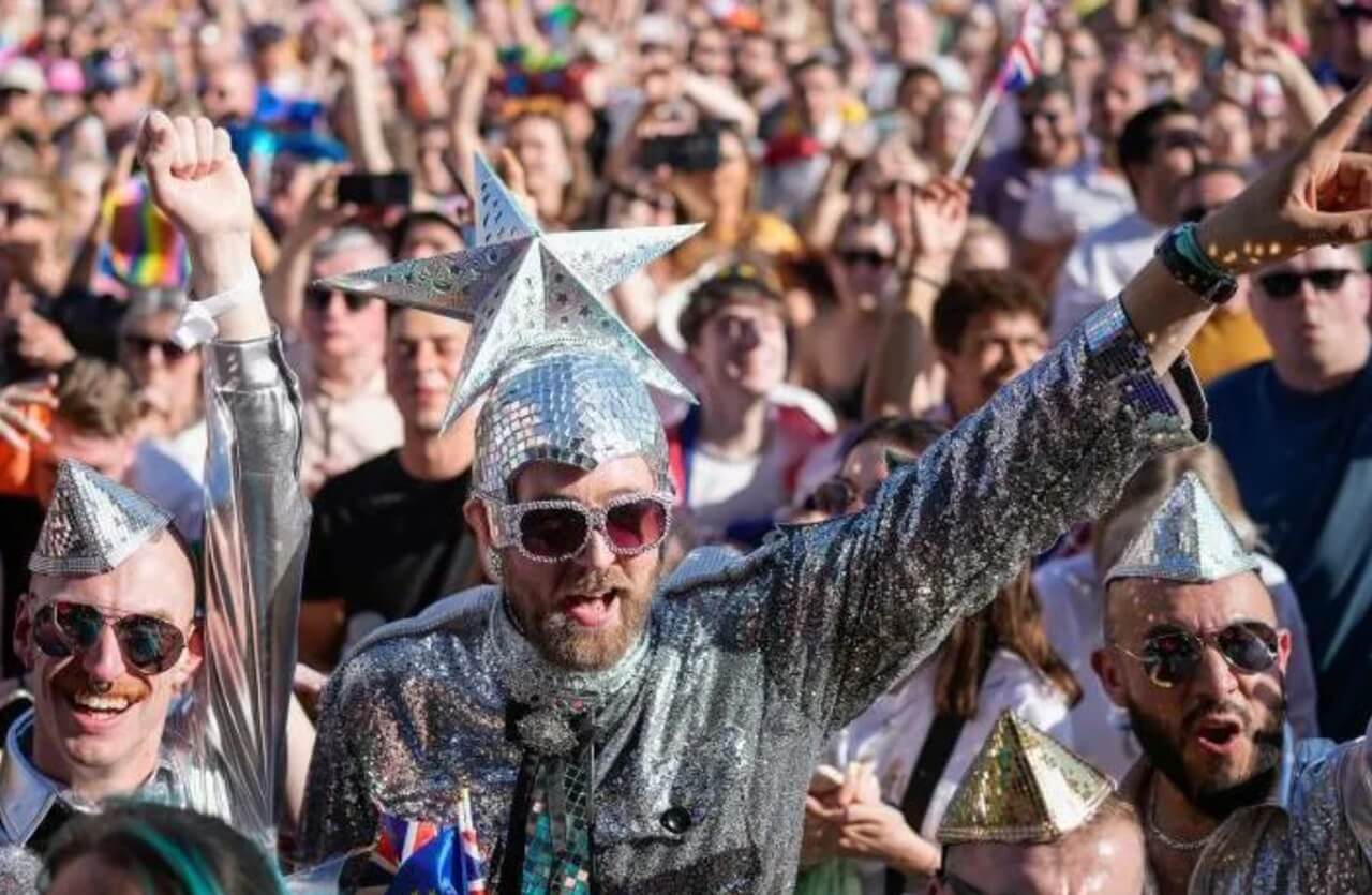 Eurovision fans in costumes waving flags at live concert.