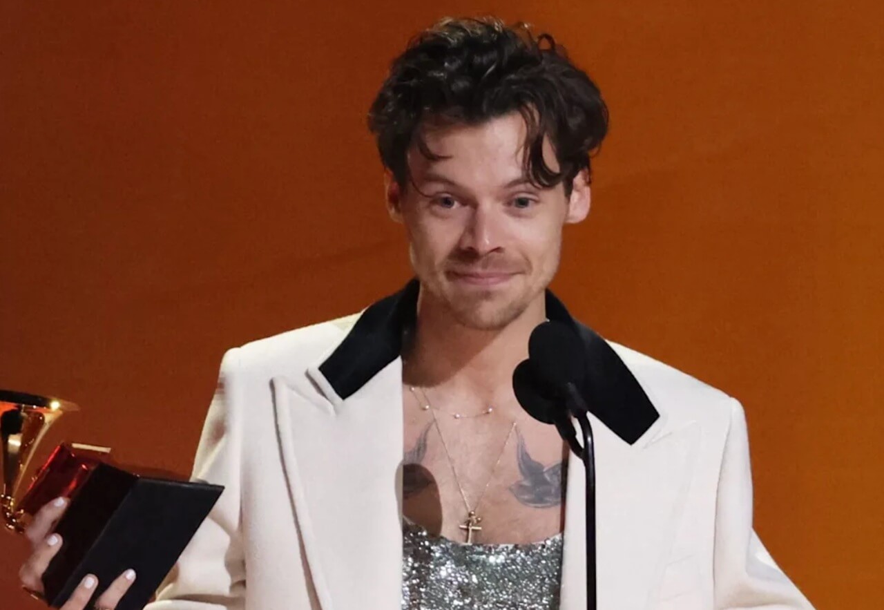 Harry Styles performing live at a concert with fans cheering in the crowd.