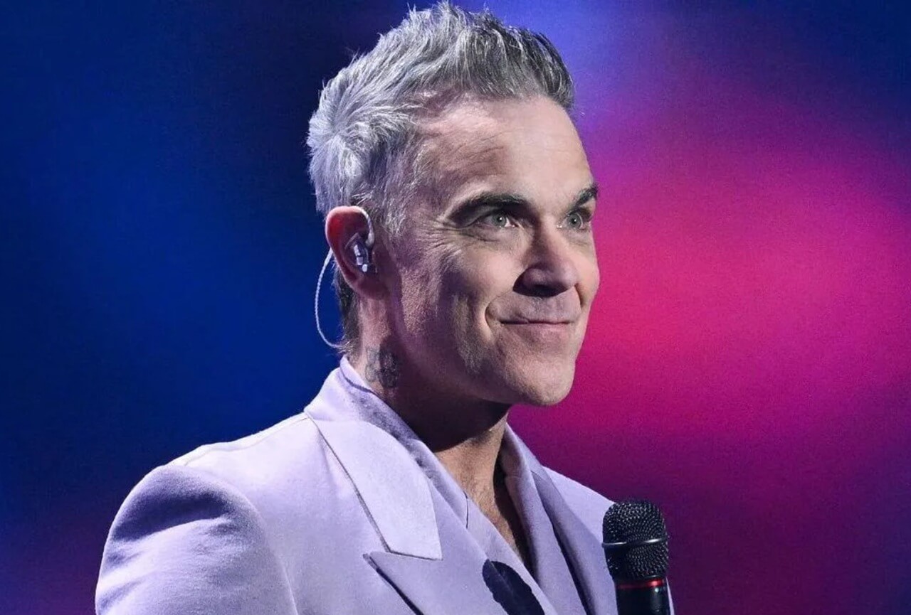 Robbie Williams celebrates success on stage during Long 90s tour.