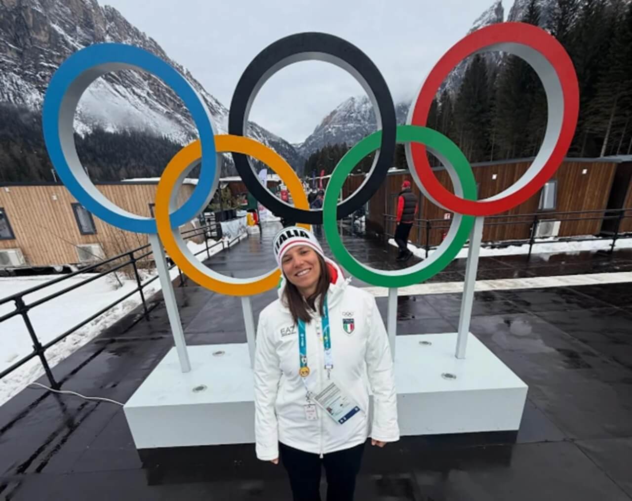 Simona De Silvestro at Winter Olympics in white Italian team jacket posing before Olympic rings.